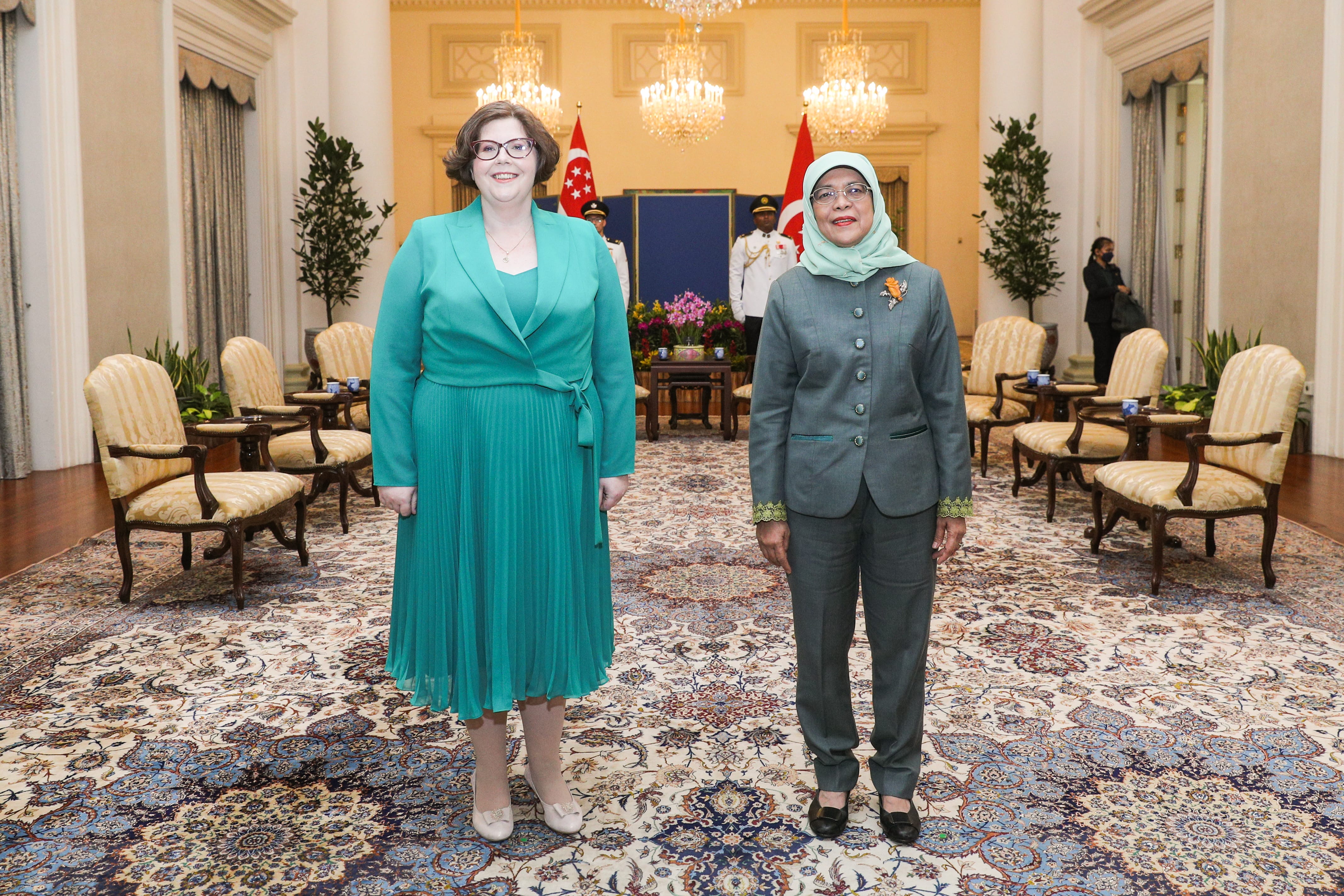 US Ambassador and Halimah Yacob pose in a room with Singapore flags, chairs and patterned carpet.